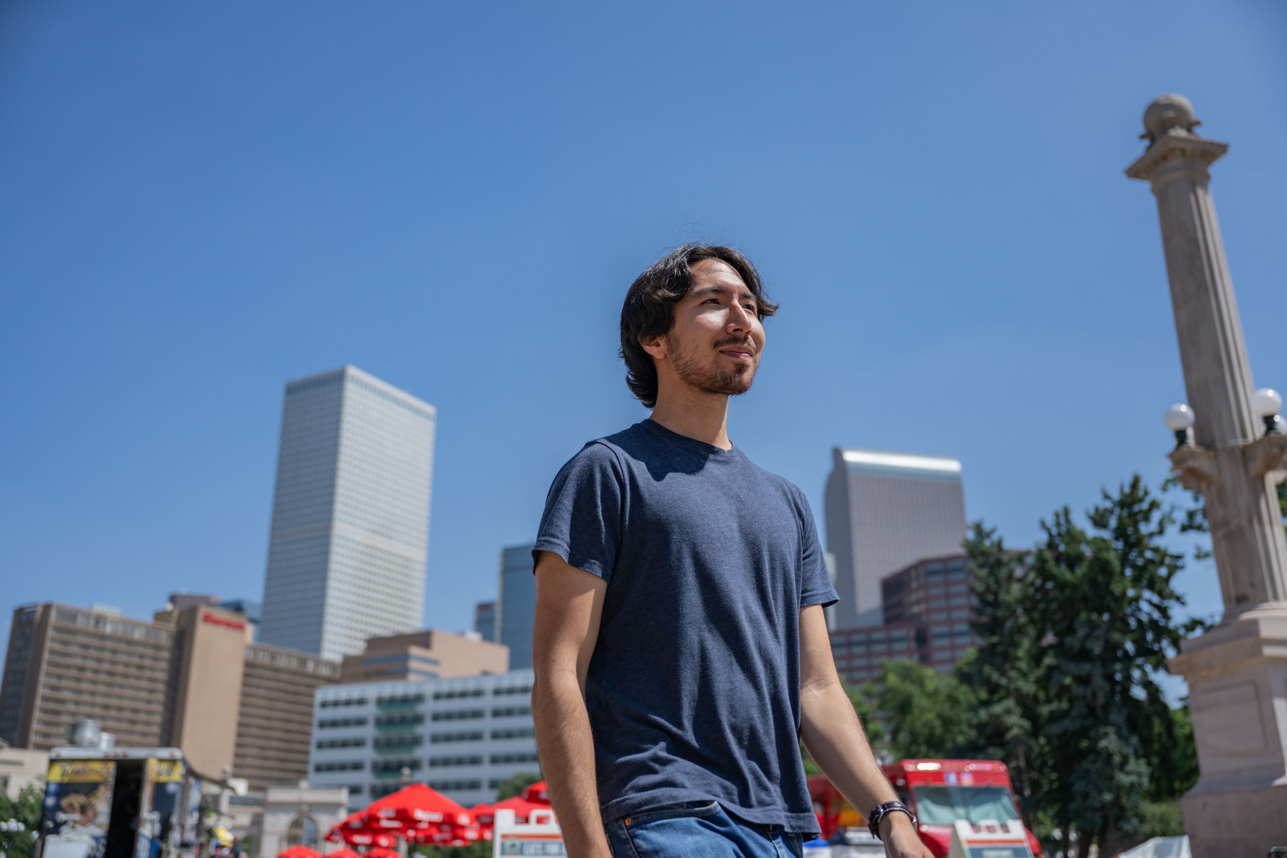 A man in a blue tee shirt walking in Capitol Hill, with the Denver Skyline visible in the background