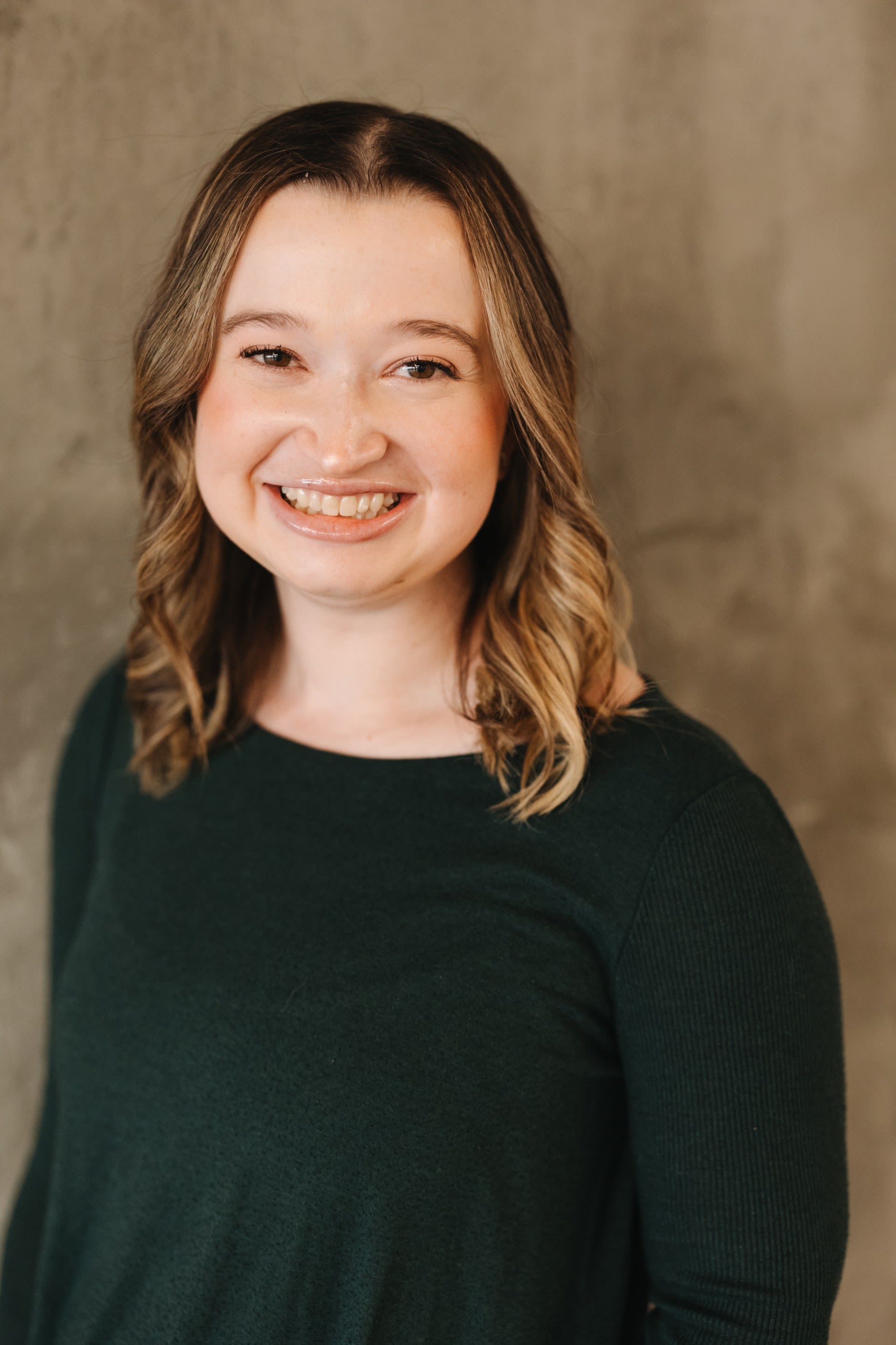 A woman in a green sweater smiling at the camera in front of a wall.