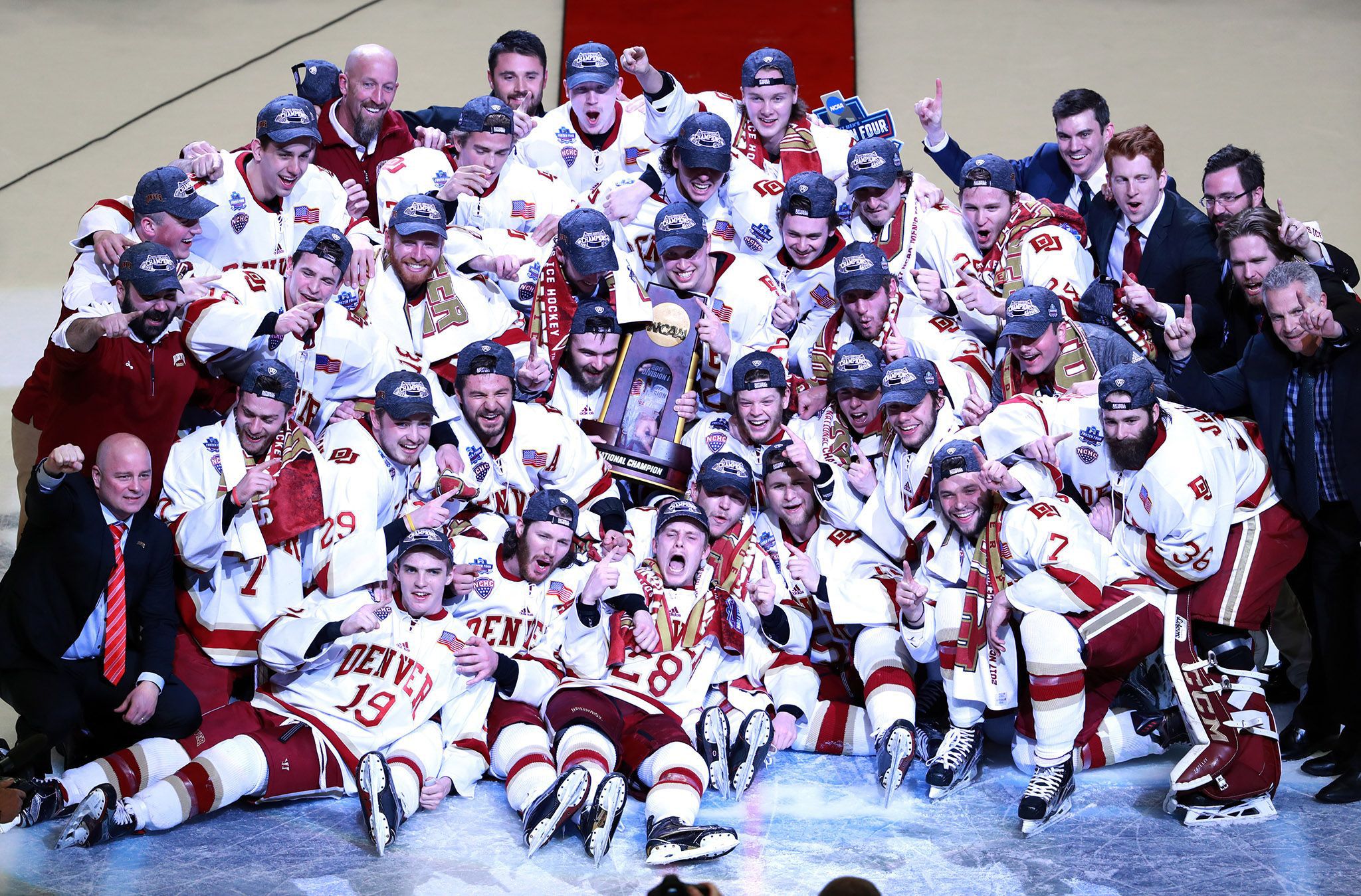 The 2017 DU men's hockey team holds up "#1" fingers on the ice in front of the NCAA Champion trophy.