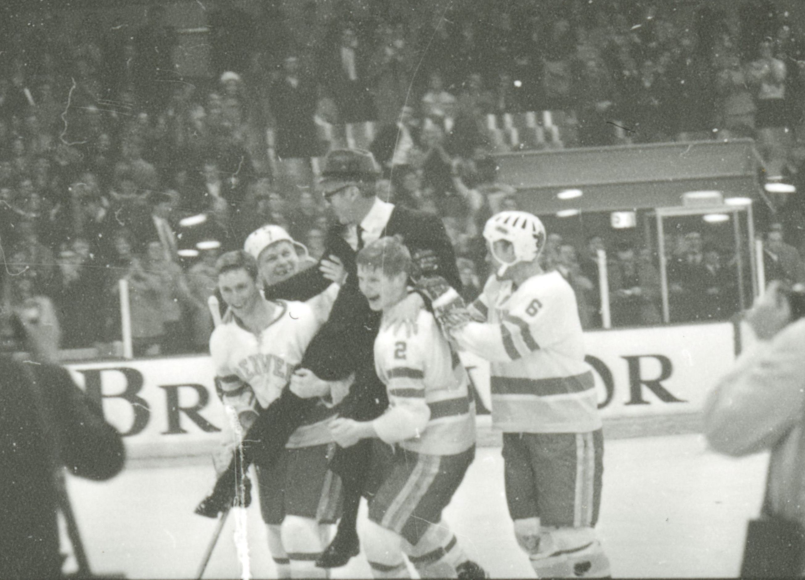 Four DU hockey players carry their coach across the ice.