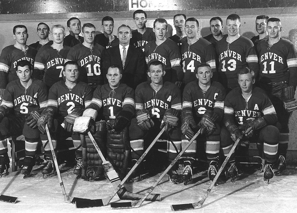Holding sticks, the University of Denver 1961 hockey team poses for a formal photo in their uniforms with the arched Denver logo.