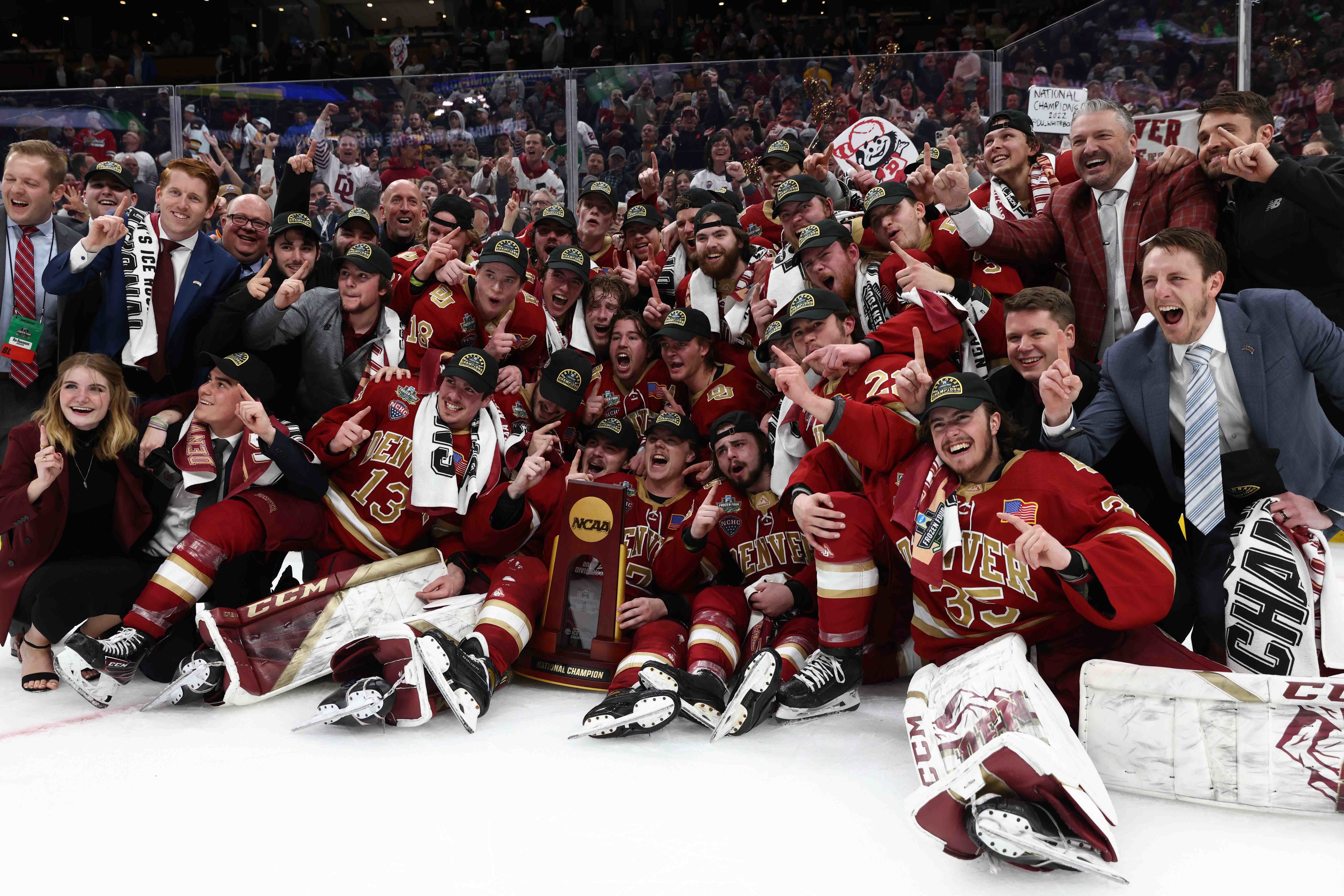 The 2022 DU men's hockey team holds up "#1" fingers on the ice in front of the NCAA Champion trophy.