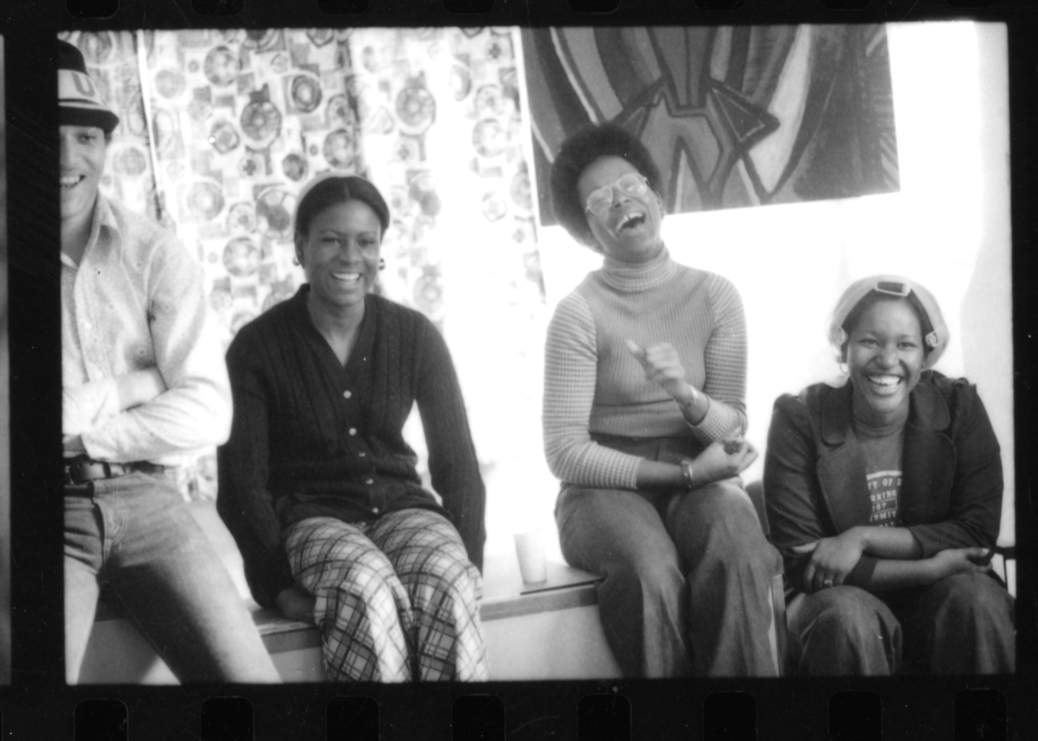 4 students are smiling and laughing in the living room of a house.