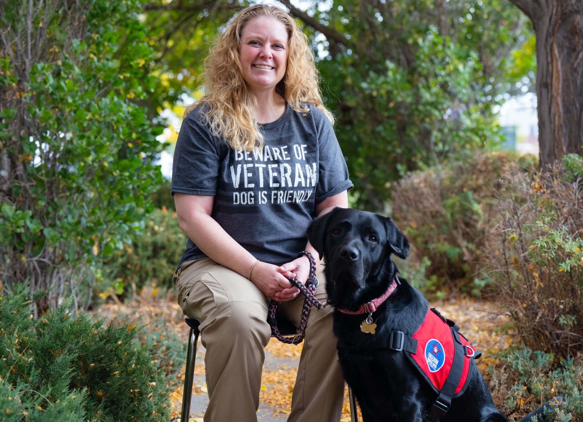 A woman sits with a black service dog.