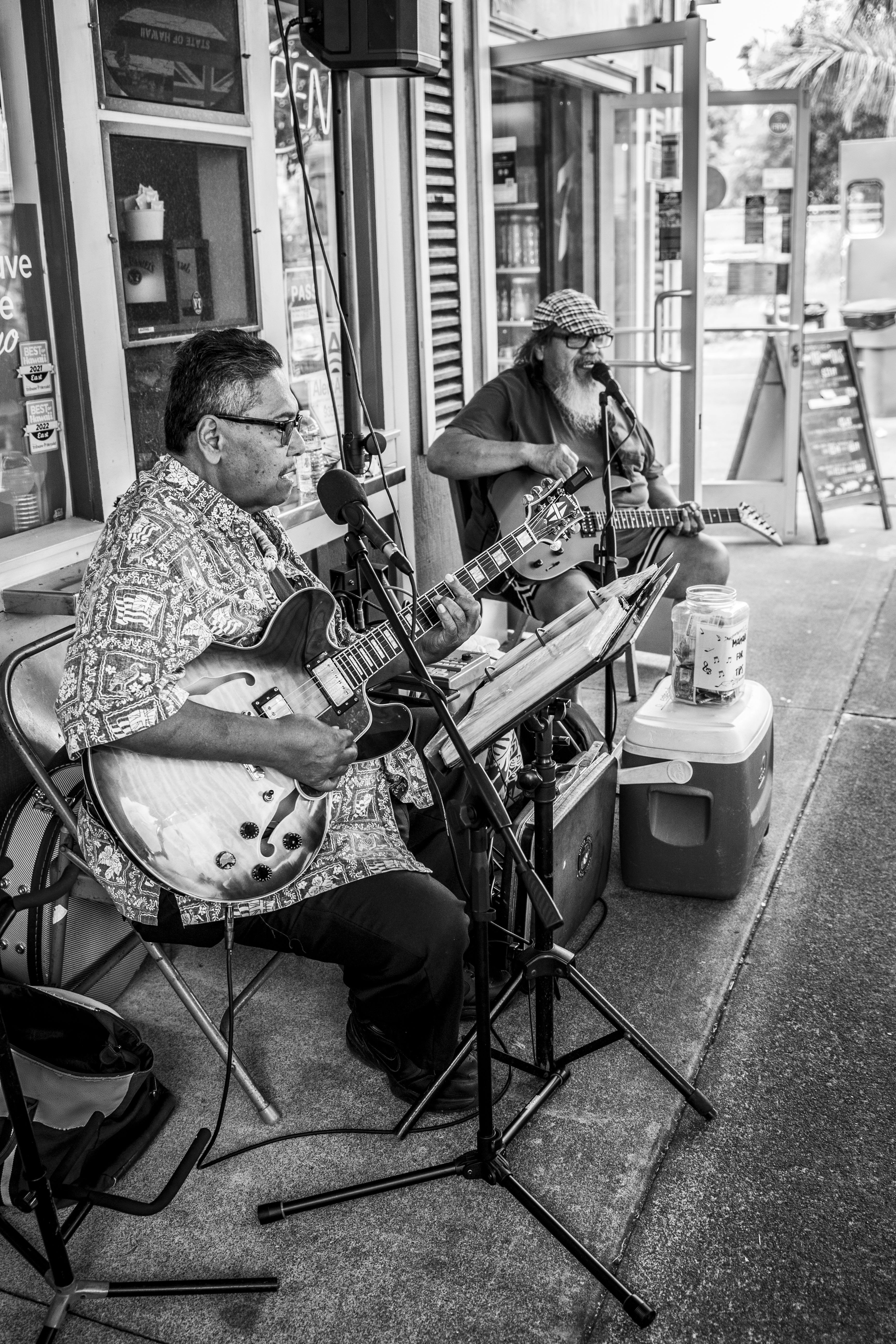 Two men play guitar outside a store front.