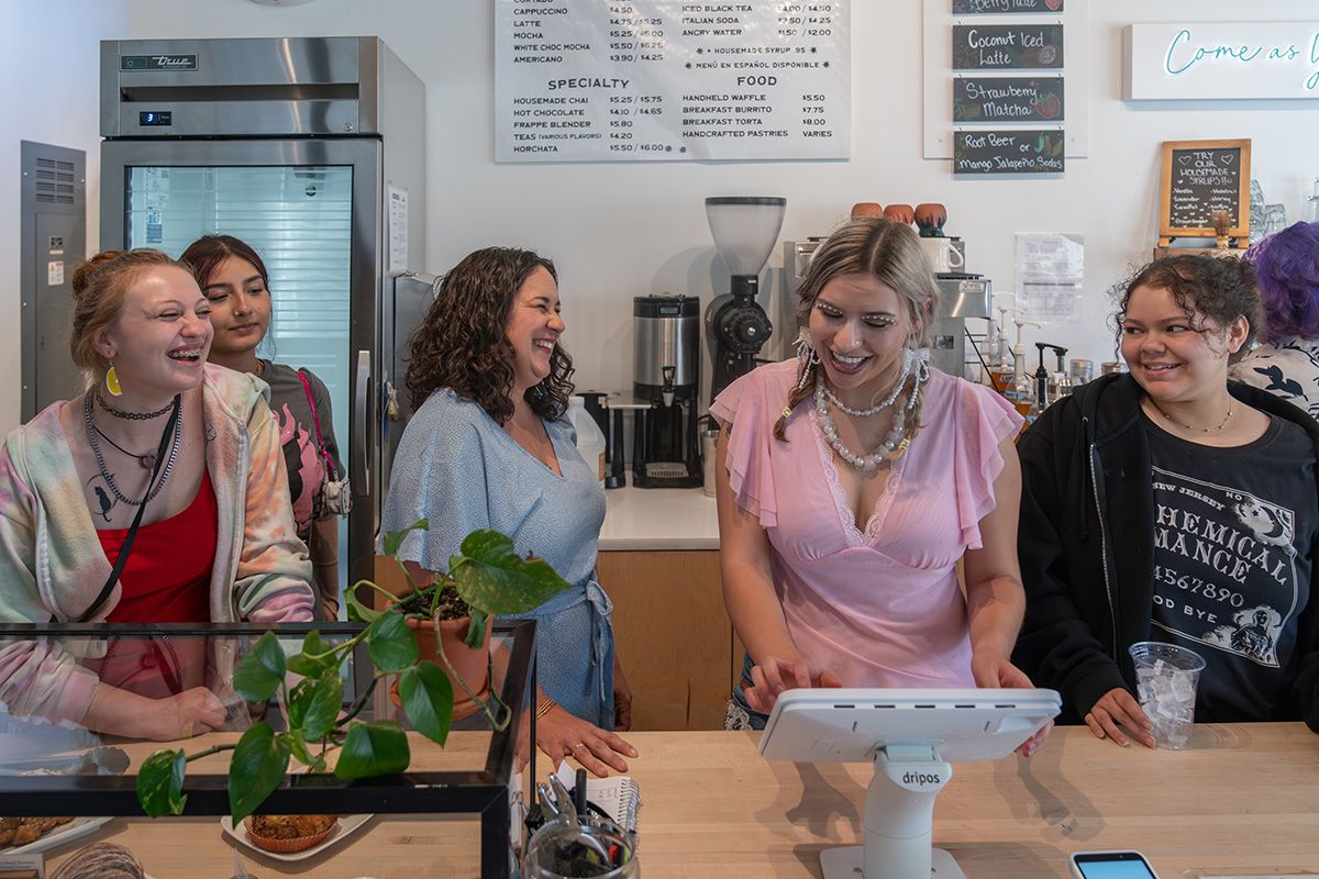 Five employees stand behind a coffee counter.