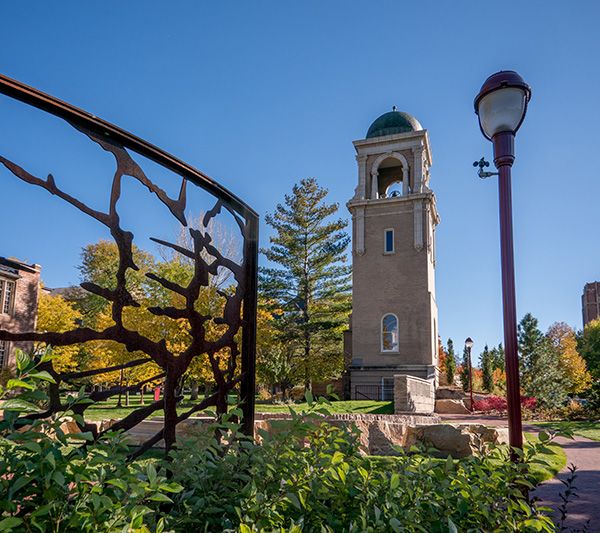 Wide-angle image of the brown wrought-iron sculpture that is part of D-U's Holocaust Memorial Social Action Site, seen against a backdrop of the Buchtel Memorial Chapel's bell tower.