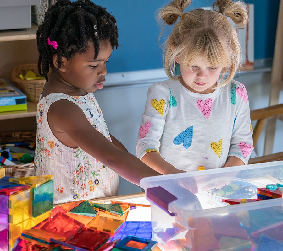 Photo of two children, a young Black girl and a young white girl, playing together with blocks in a classroom.