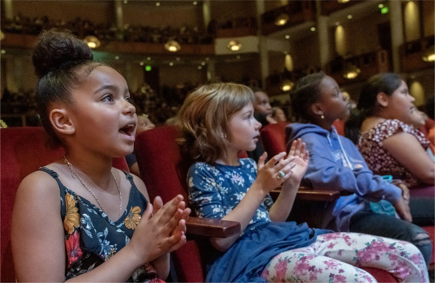 Four children sitting in a theater applauding.