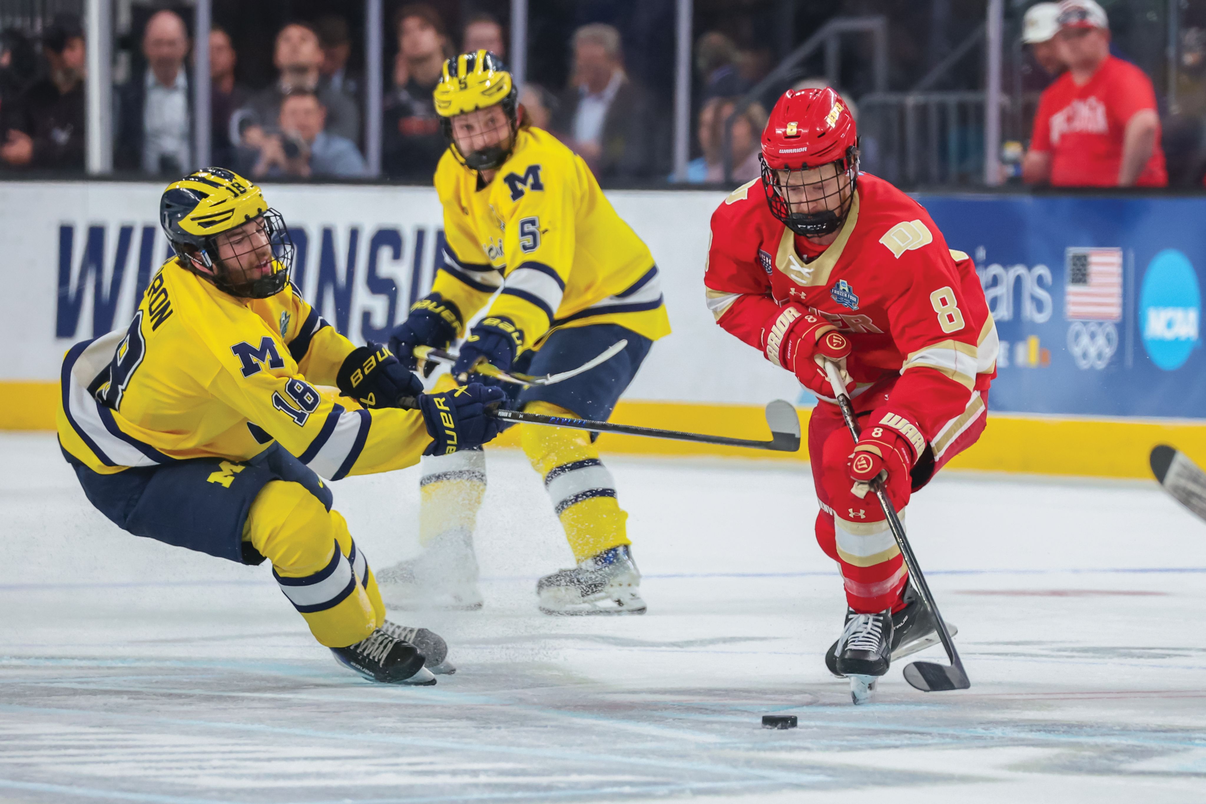 DU hockey player with a puck while playing Michigan hockey players