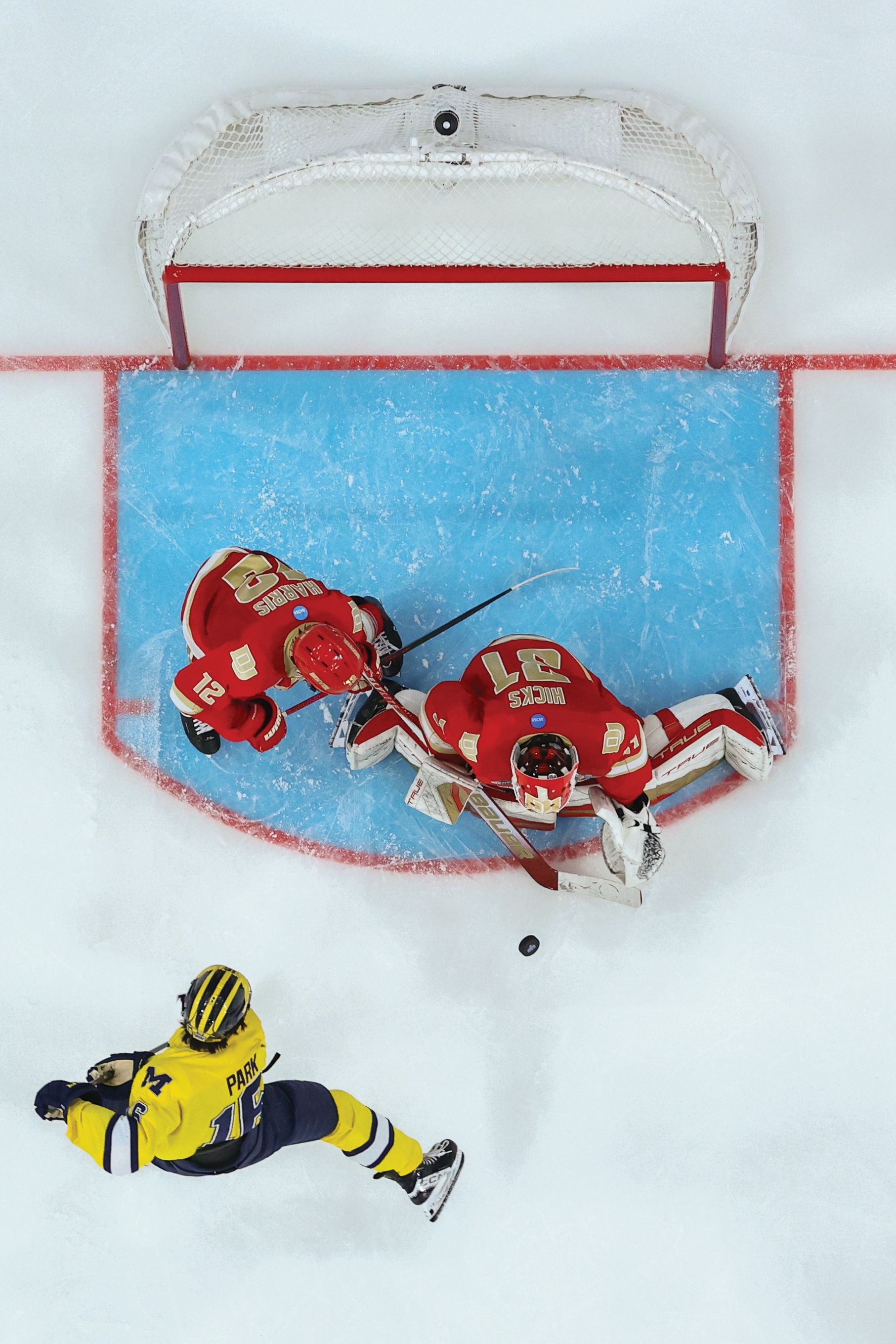 three hockey players playing hockey in front of a hockey goal