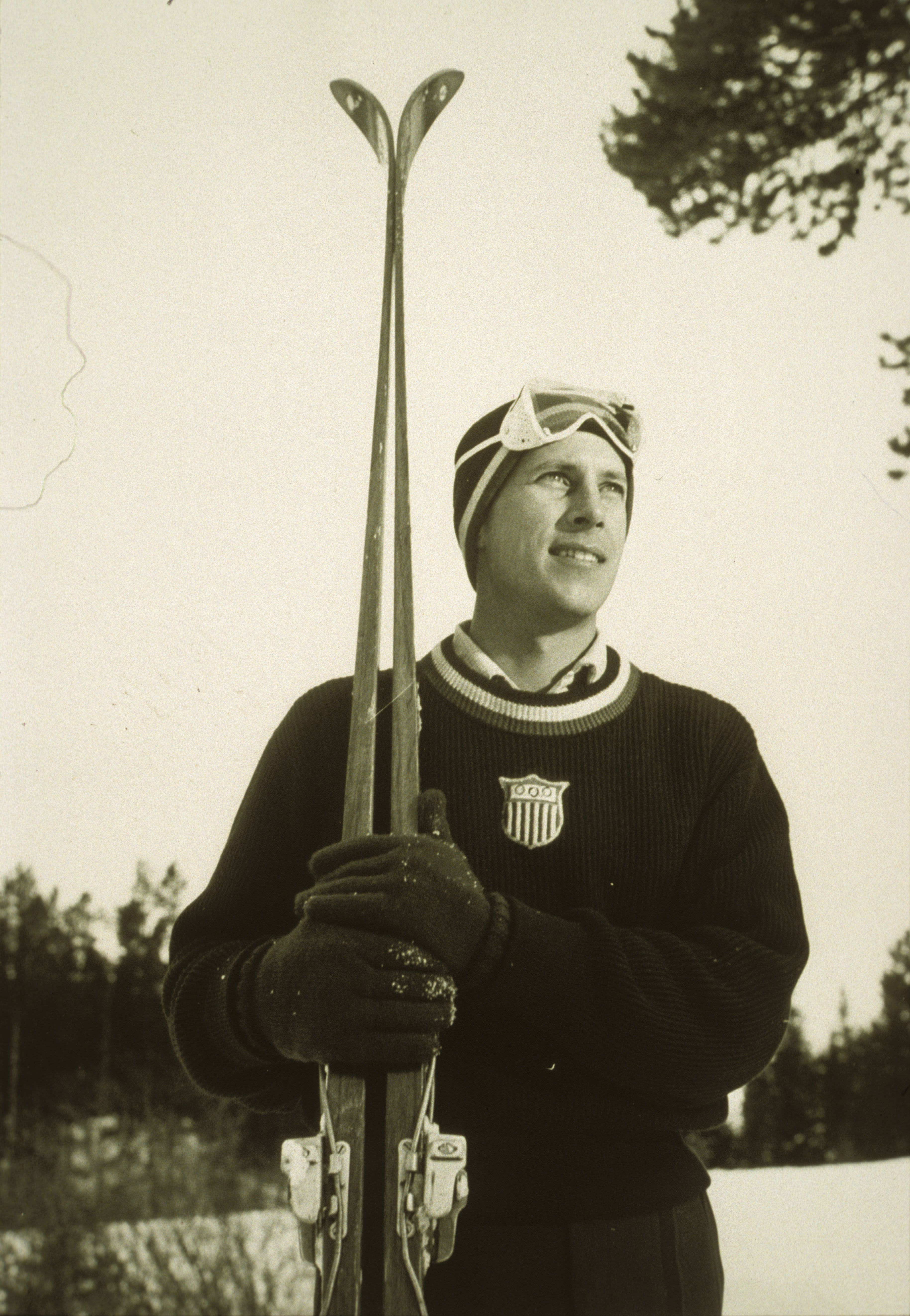Marvin Crawford poses for a portrait while holding his skis over his right shoulder and wearing a ski sweater, hat and goggles. 