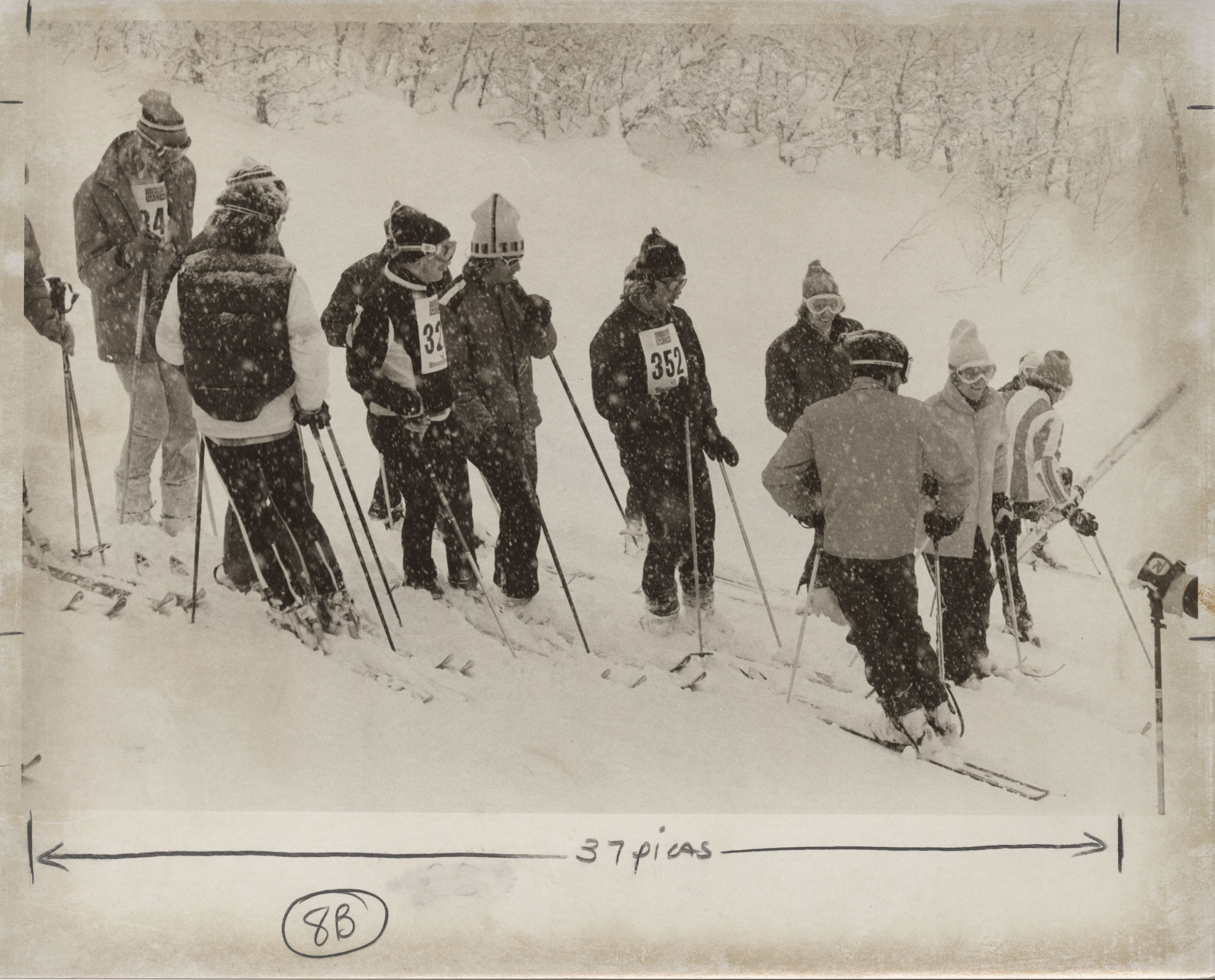 DU skiers stand on a hill with their ski race bibs on under heavy snow