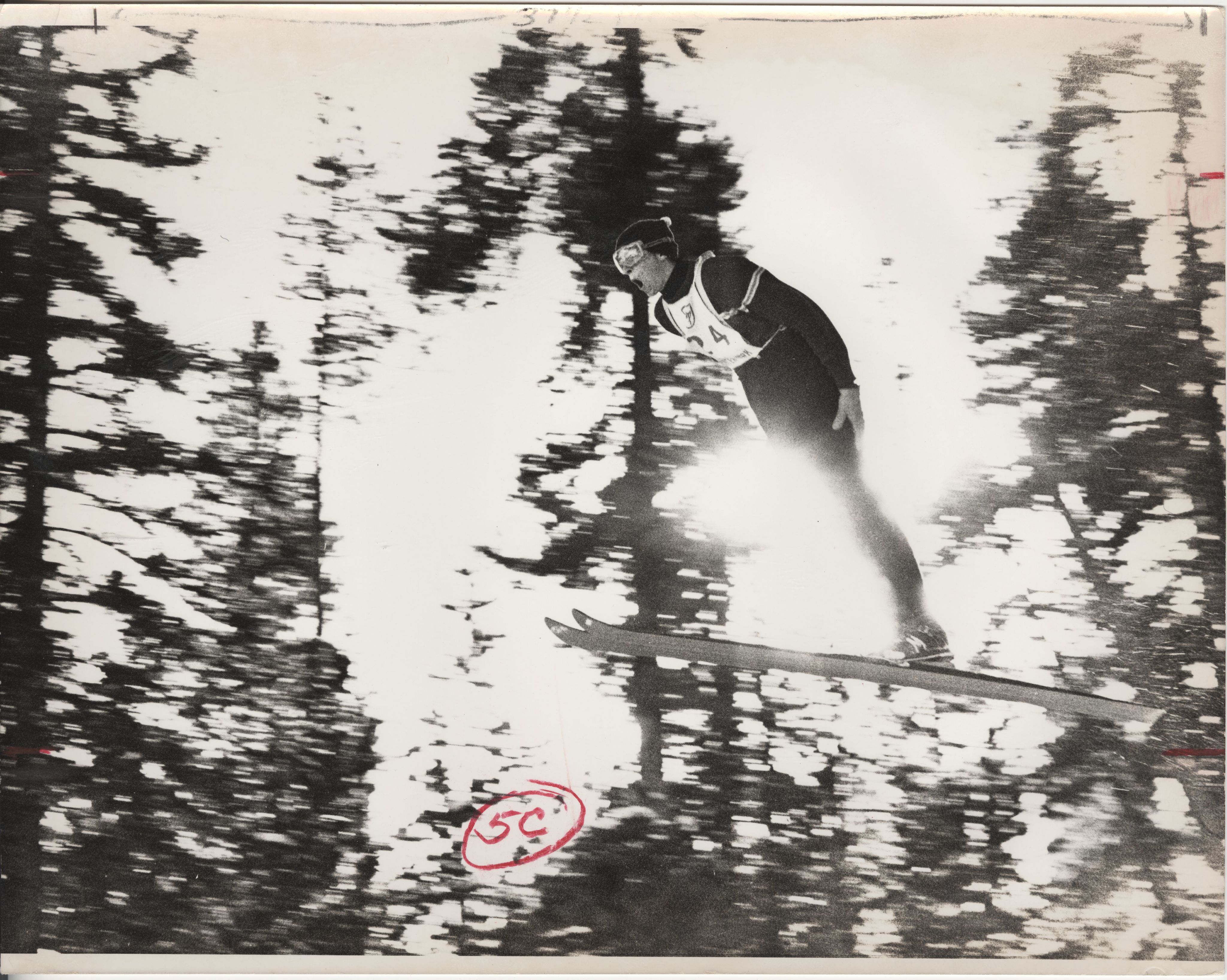 A male ski jumper flies through the air with his arms tucked to his side and mouth open wide