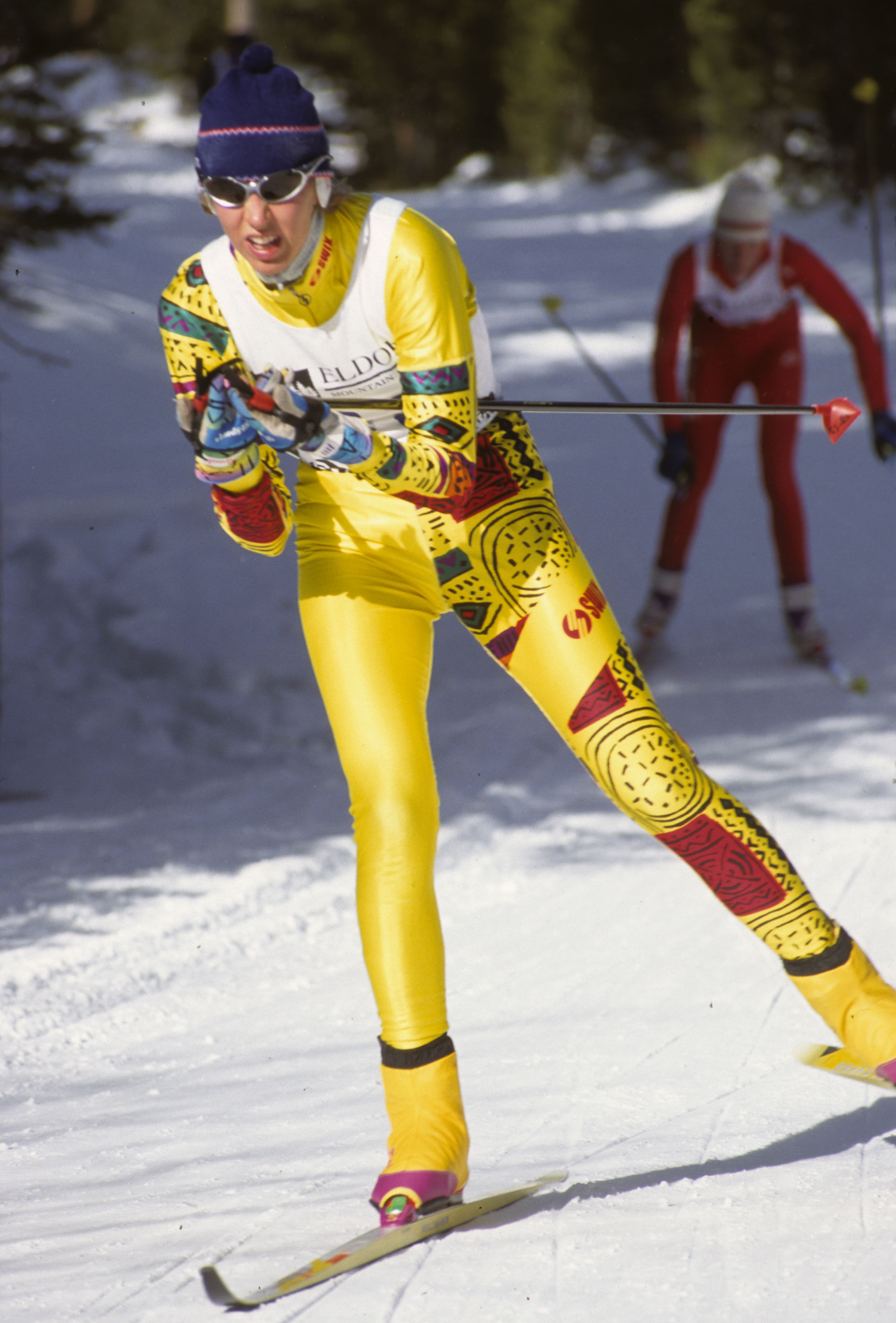 Carolina Barthelson races in cross country with a yellow ski suit and a skier over her left shoulder