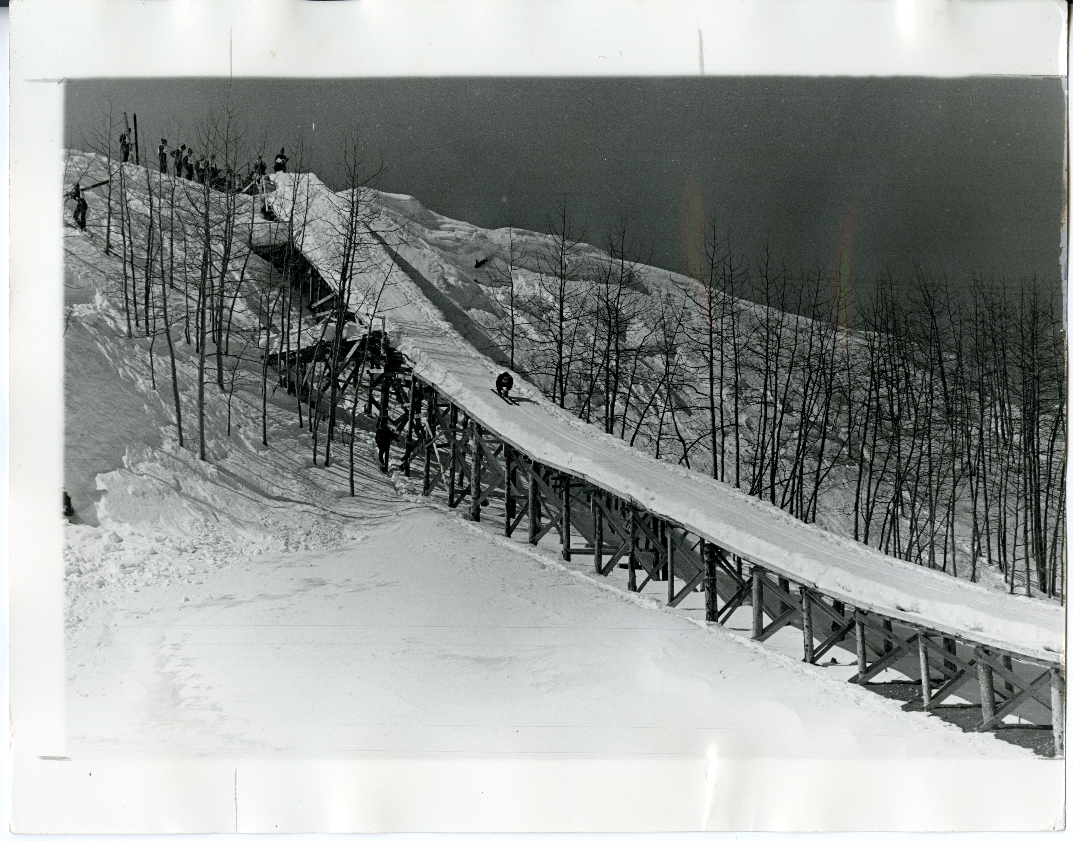 A skier is midway down a large wooden structured ski jump down a large mountainside.
