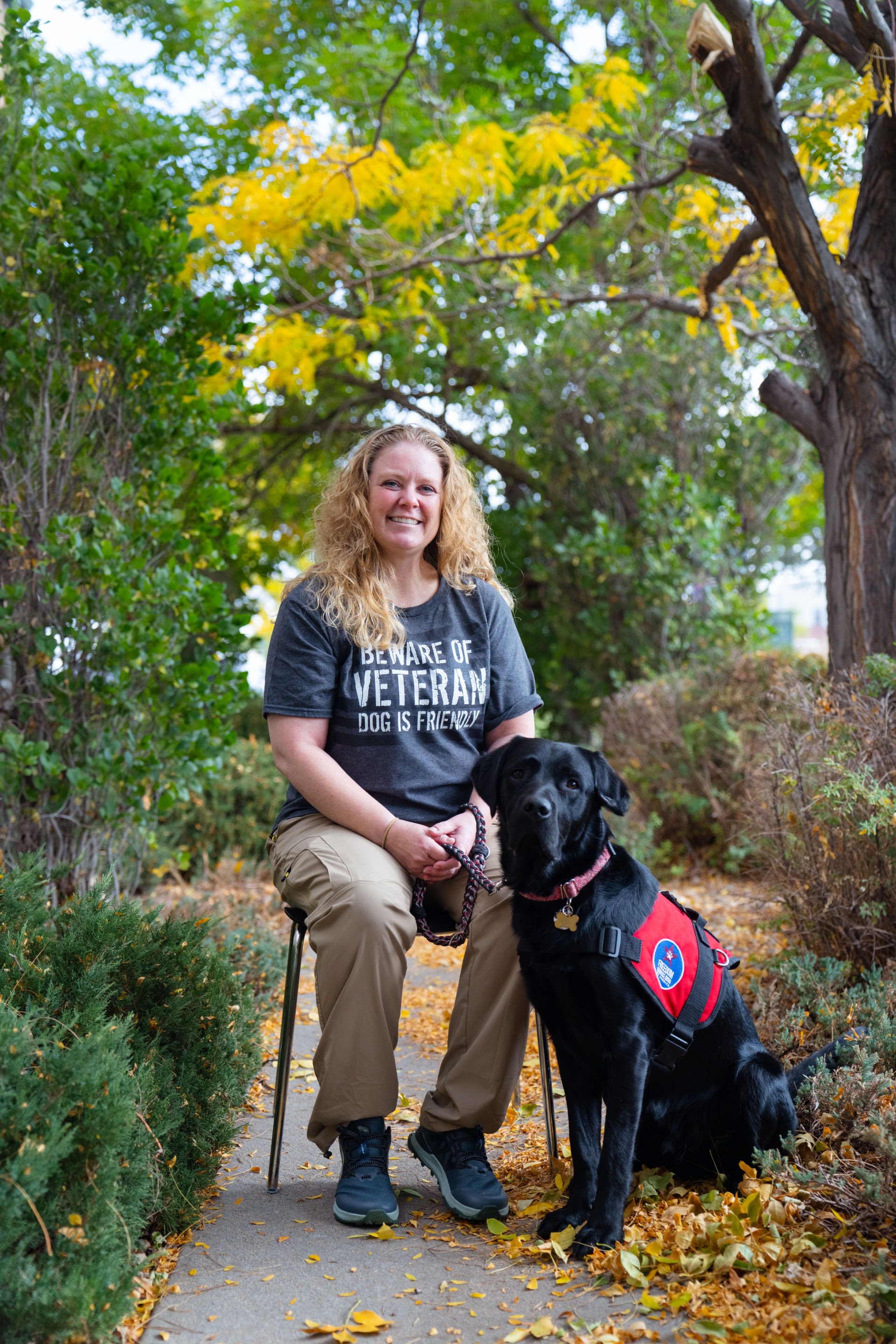 A woman sits with a black service dog.