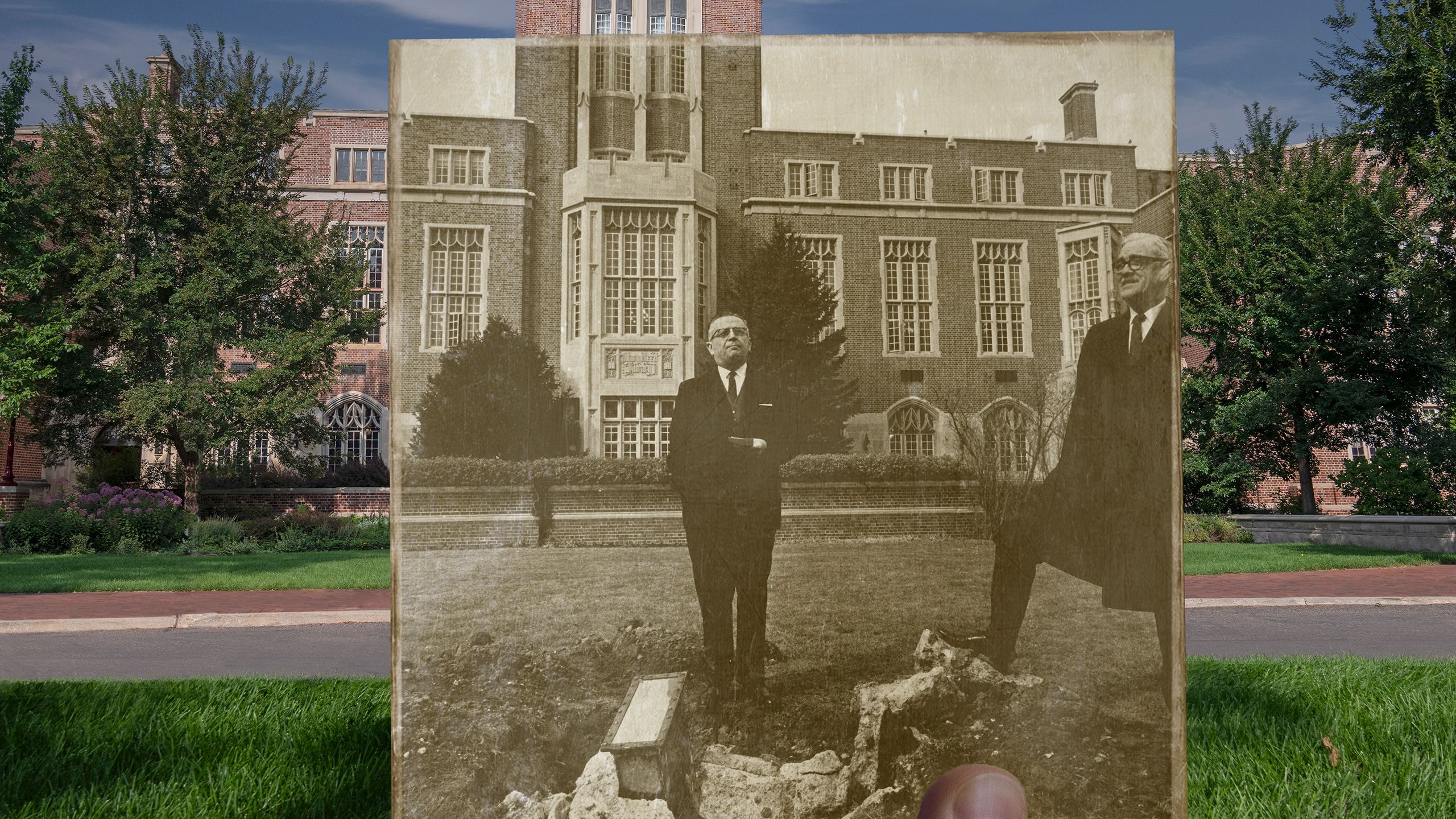 Historic photo of two men digging up a time capsule, with modern Mary Reed Building in the background.