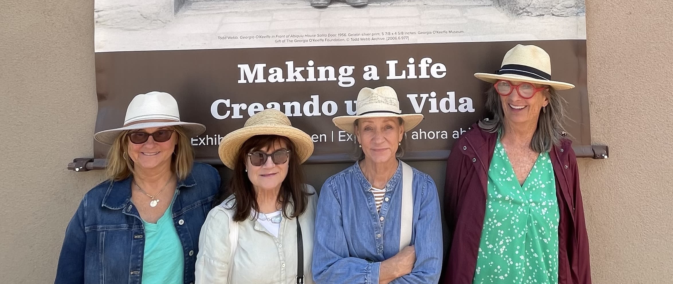 Four women in sun hats stand in front of a stucco building.
