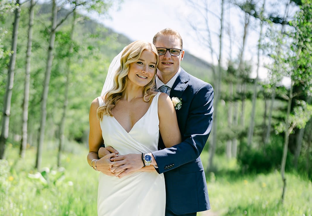 Samantha and Joe in a wedding dress and suit outside in a green forest.