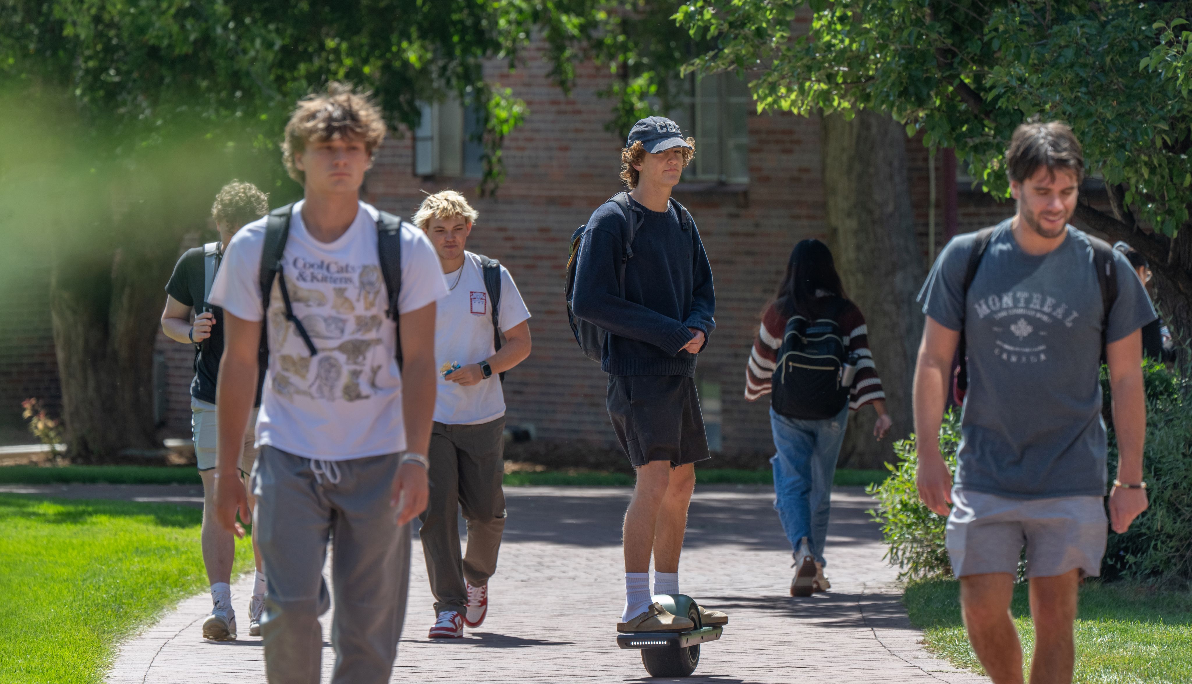 A group of young male DU students walk and skateboard during a nice, sunny day on campus.