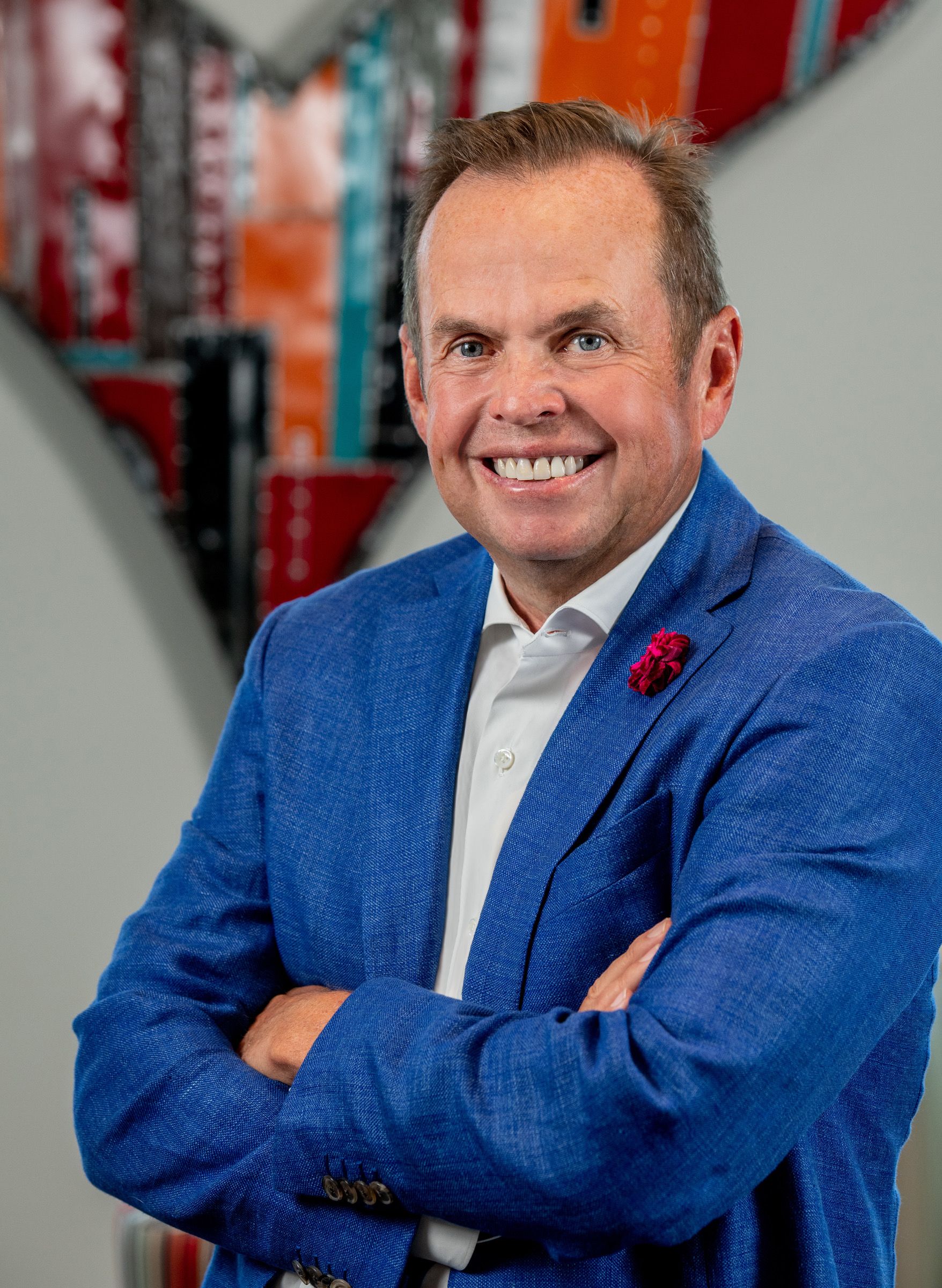 Pat Hammil in a blue coat jacket and multi-colored art in the background