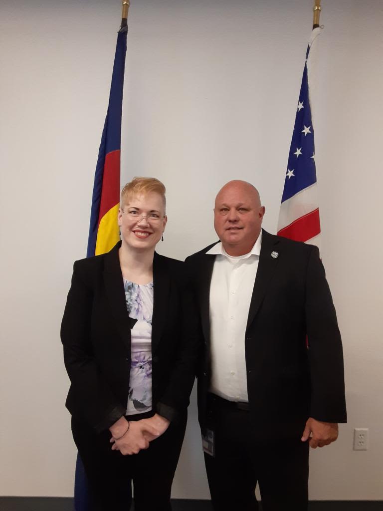 Sarah Draney with a man in front of a state and national flag.