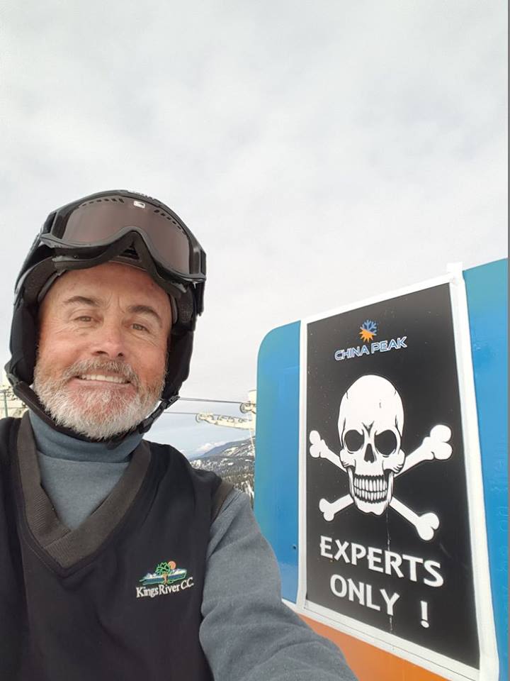 Photo of Michael Gerosa wearing a ski helmet and goggles, posing next to a sign that says "Experts only" next to a skull and crossbones.