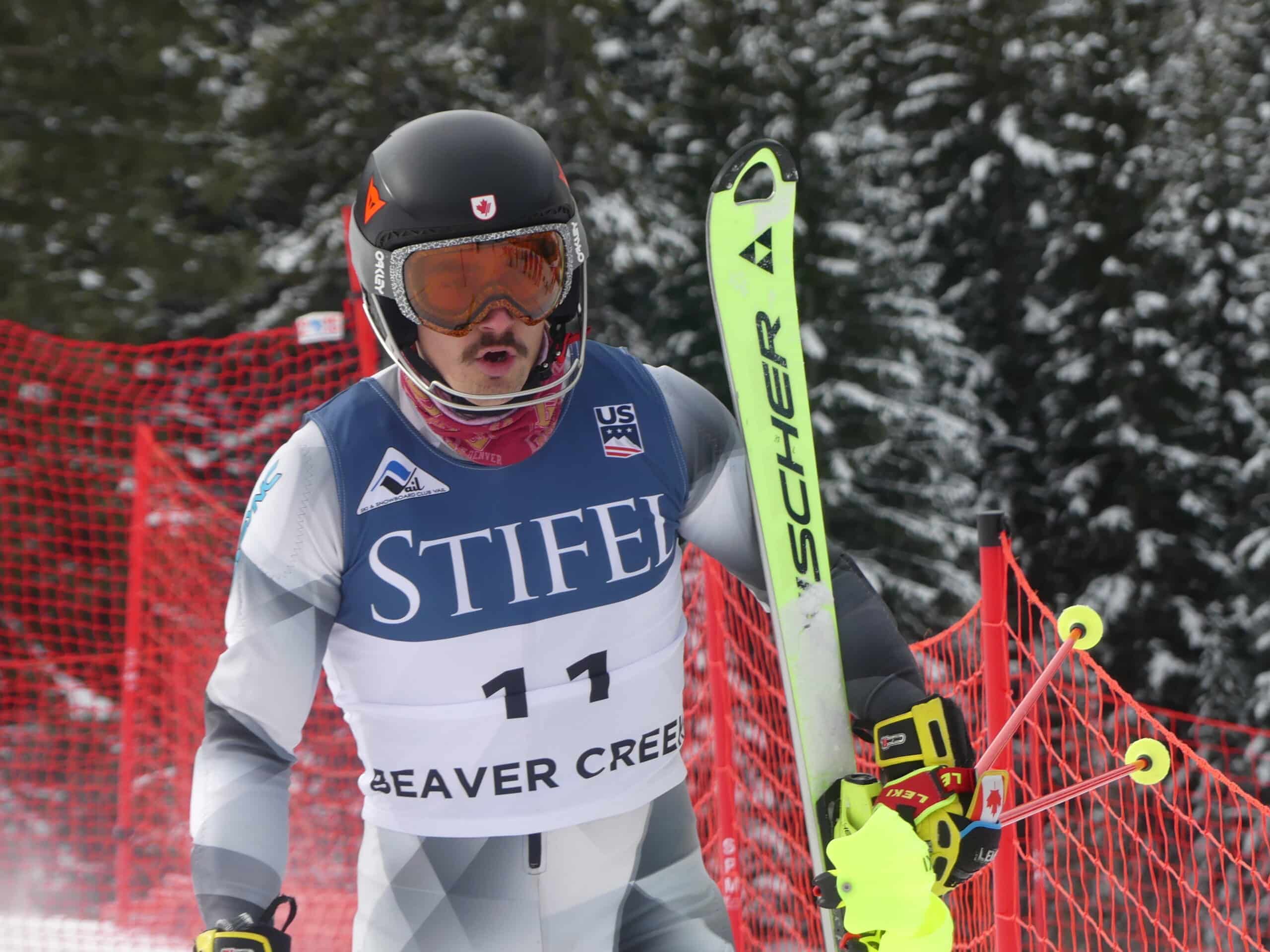 Simon Fournier, decked out in competitive ski gear, holds a set of skis.
