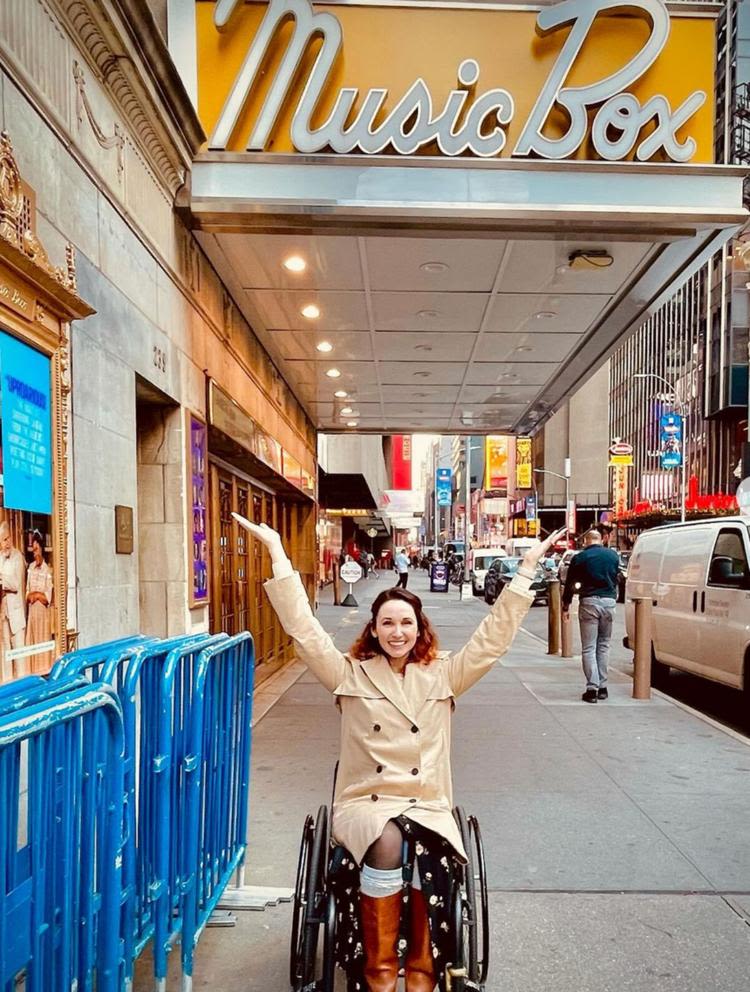 Jenna Bainbridge sits in a wheelchair under the marquee sign of the Music Box Theatre.