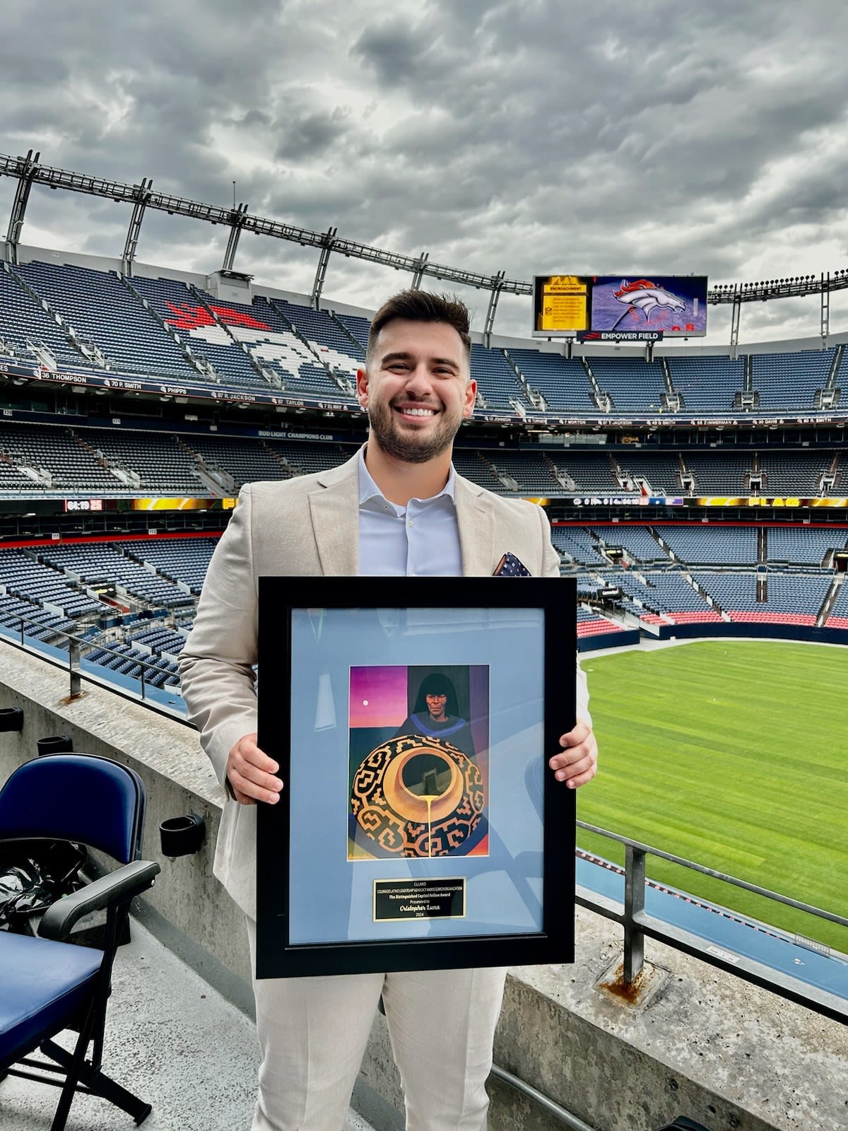 A photo of Christopher Luna holding an award with Coors Field visible in the background