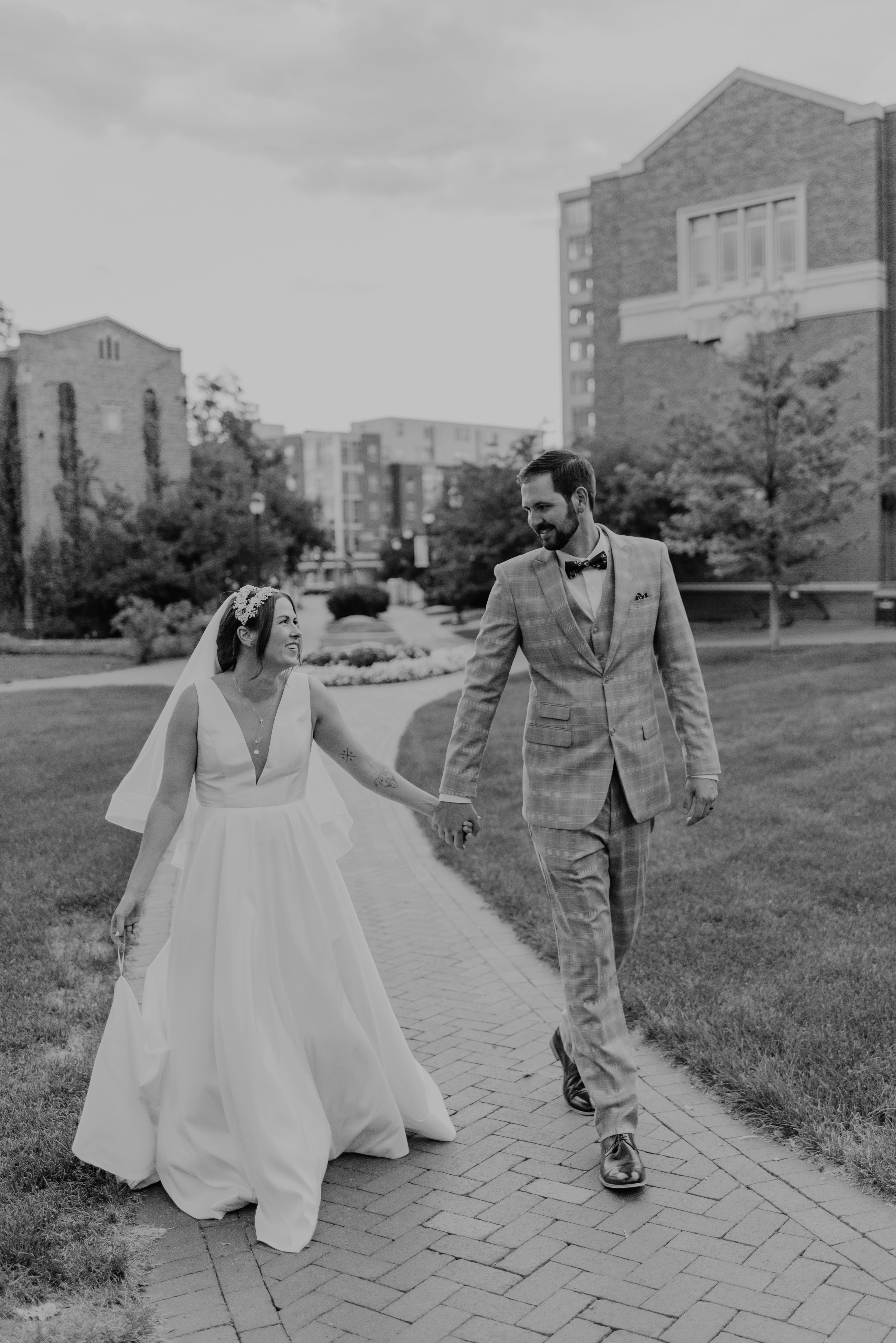 a bridge and groom hold hands as they walk on the DU campus paths